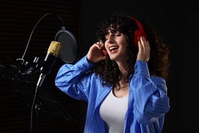 Photo of Vocalist with headphones singing into microphone in professional record studio