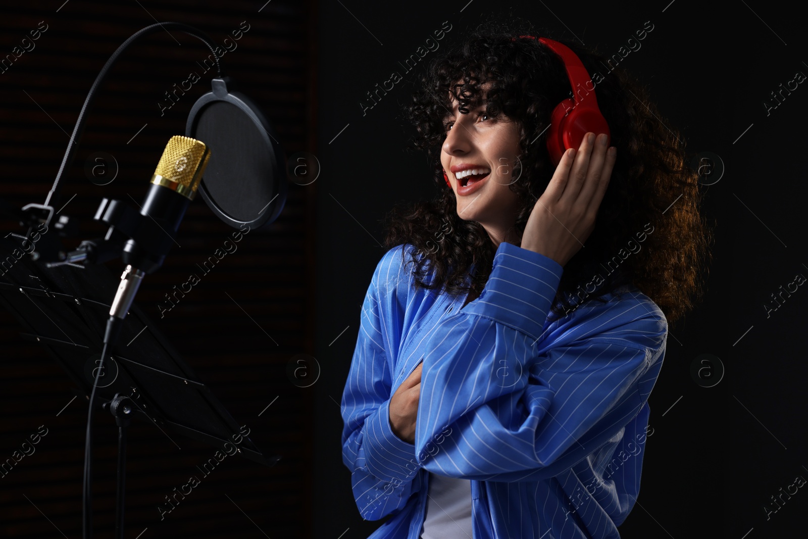 Photo of Vocalist with headphones singing into microphone in professional record studio