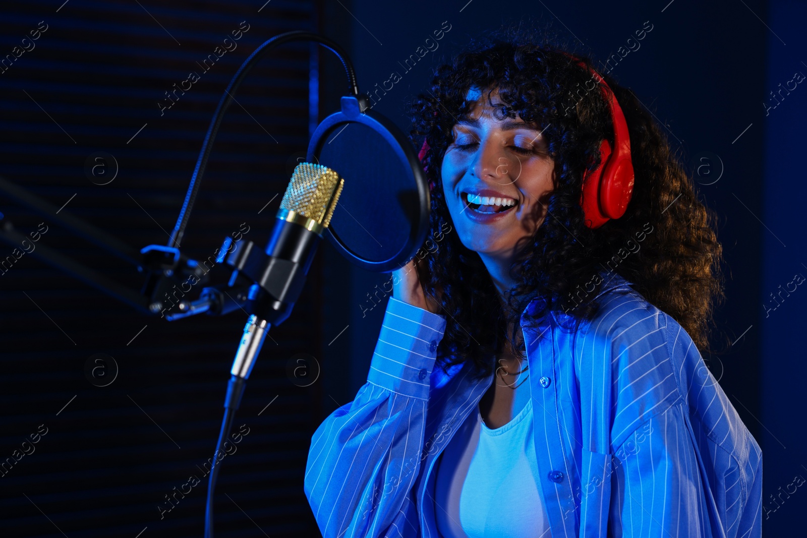 Photo of Vocalist singing into microphone in professional record studio with color lights