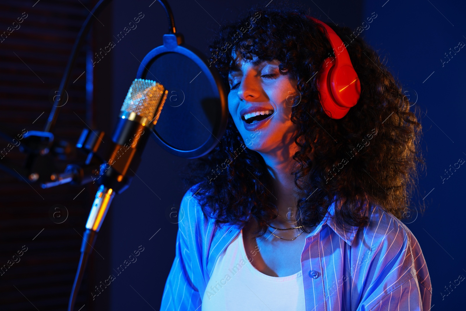 Photo of Vocalist singing into microphone in professional record studio with color lights