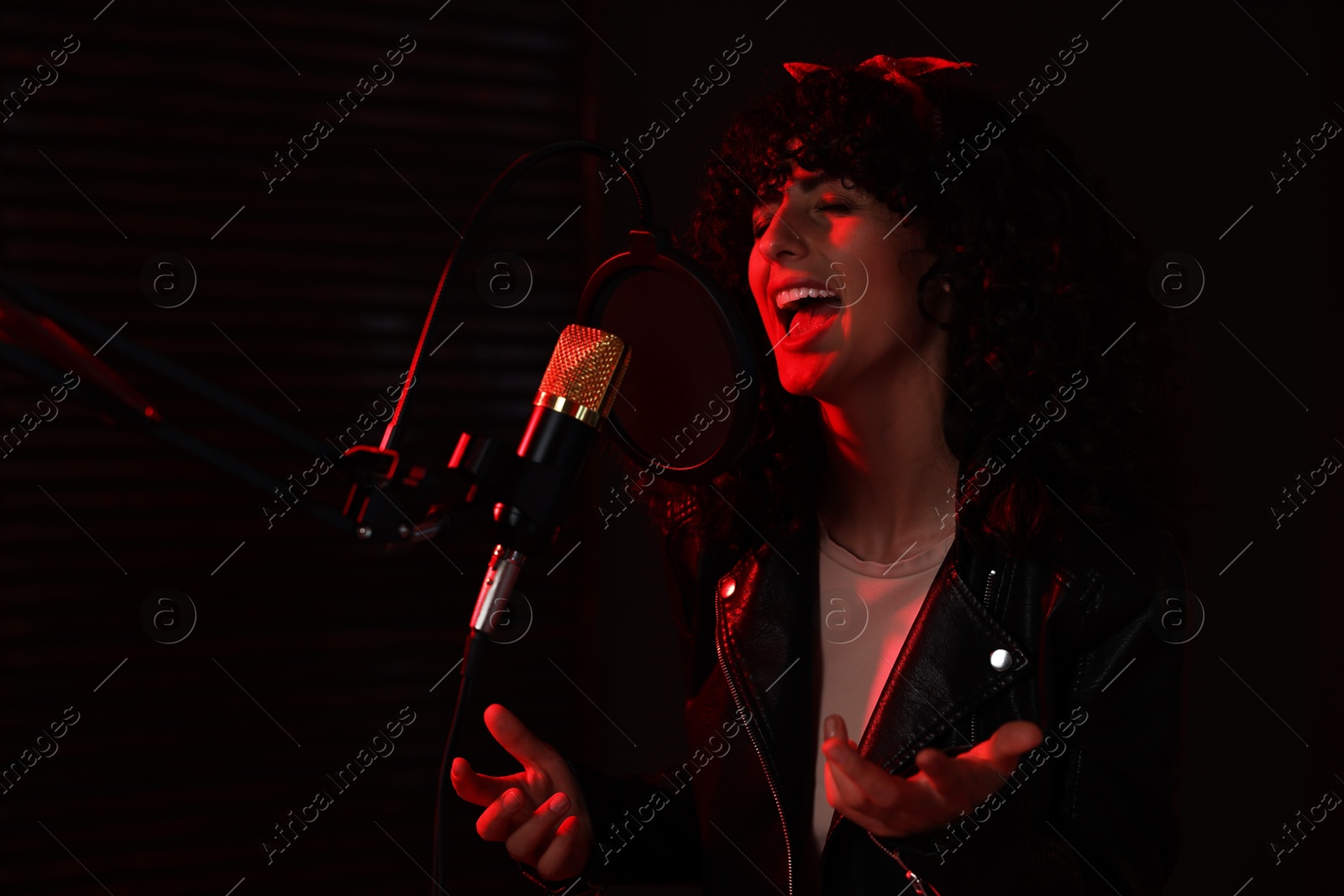 Photo of Vocalist singing into microphone in professional record studio with red light