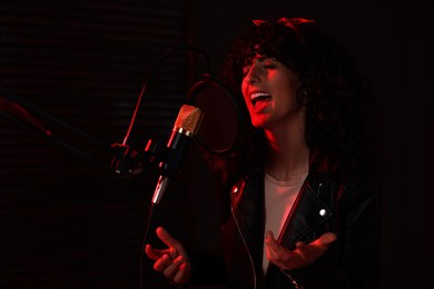 Vocalist singing into microphone in professional record studio with red light