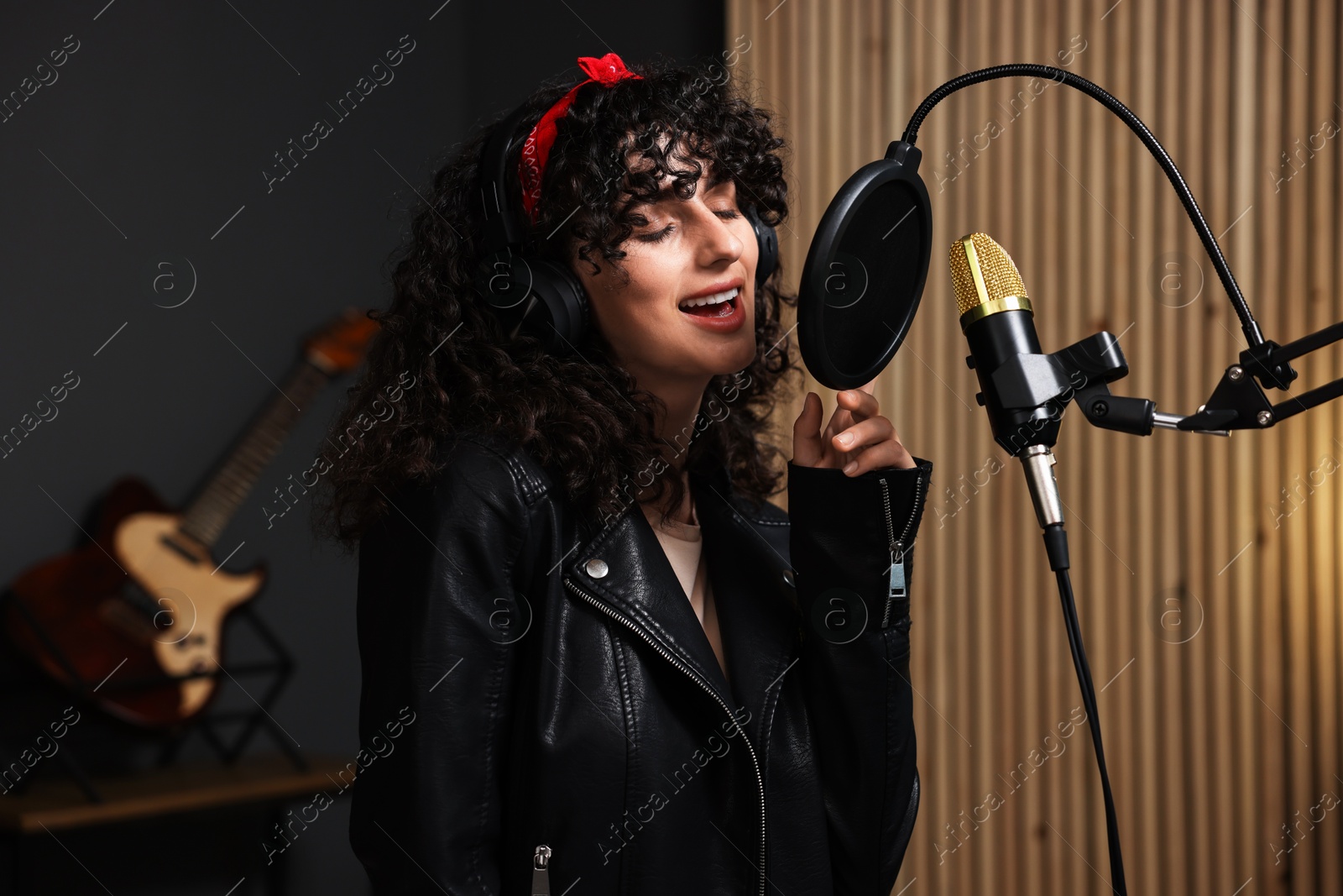 Photo of Vocalist with headphones singing into microphone in professional record studio