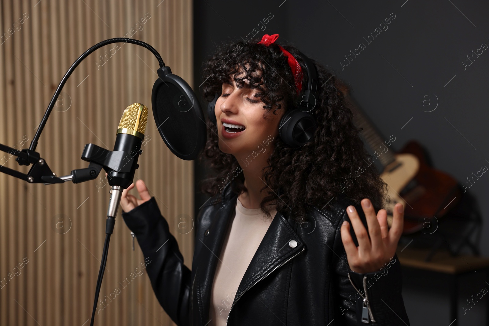 Photo of Vocalist with headphones singing into microphone in professional record studio