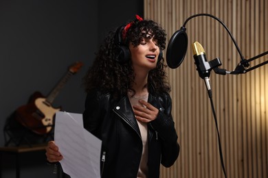 Photo of Singer wearing headphones recording song in professional studio