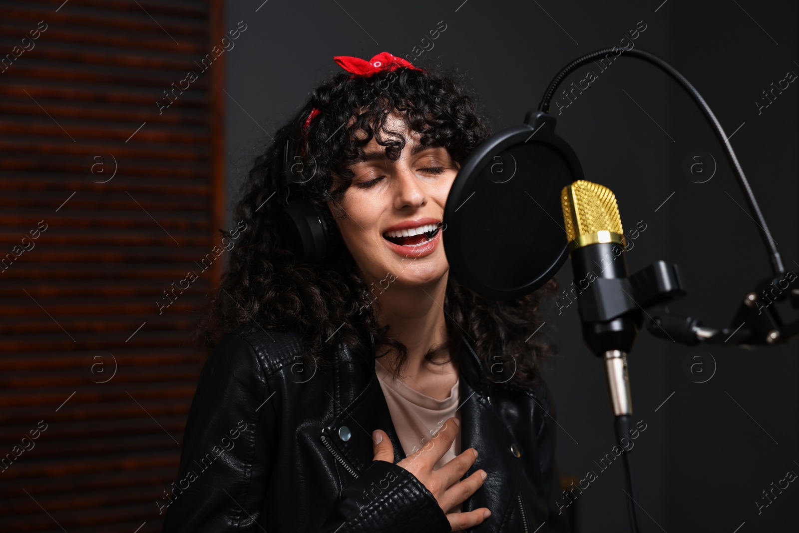 Photo of Woman wearing headphones singing into microphone in professional record studio