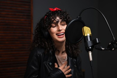 Photo of Woman wearing headphones singing into microphone in professional record studio