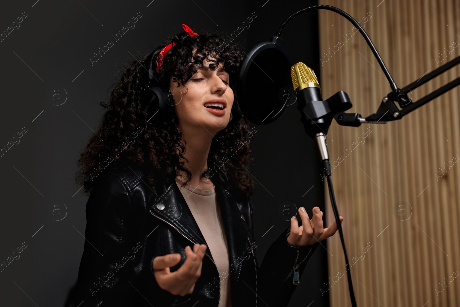 Photo of Woman wearing headphones singing into microphone in professional record studio