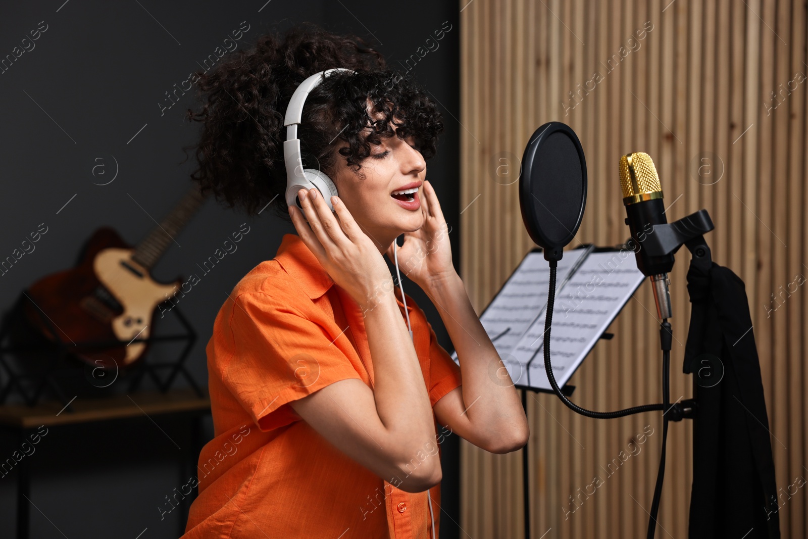 Photo of Vocalist with headphones singing into microphone in professional record studio