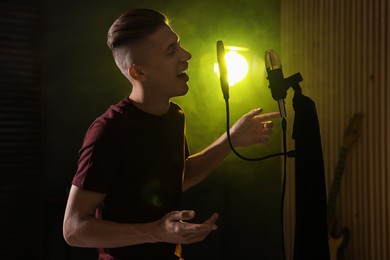 Photo of Vocalist singing into microphone in professional record studio with smoke and lights