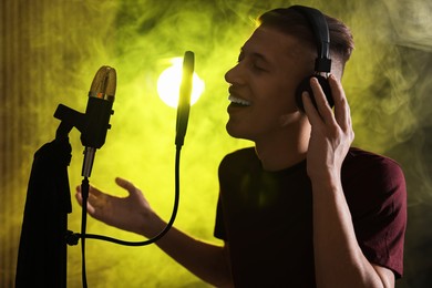 Photo of Vocalist wearing headphones singing into microphone in professional record studio with smoke and lights