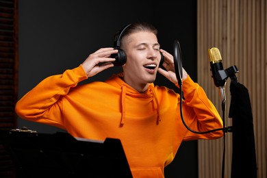 Man wearing headphones singing into microphone in professional record studio