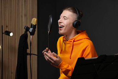 Man wearing headphones singing into microphone in professional record studio