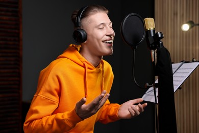 Photo of Man wearing headphones singing into microphone in professional record studio