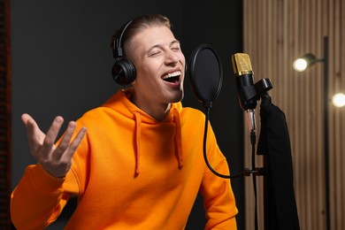 Man wearing headphones singing into microphone in professional record studio