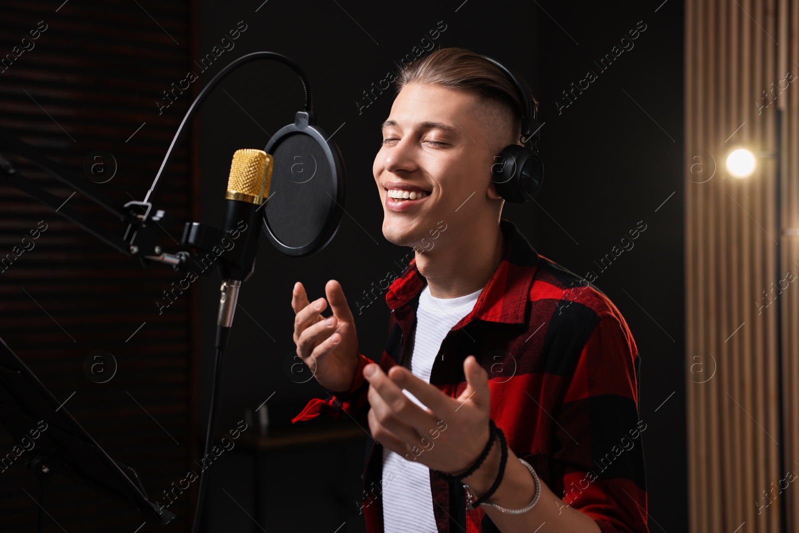 Photo of Vocalist with headphones singing into microphone in professional record studio