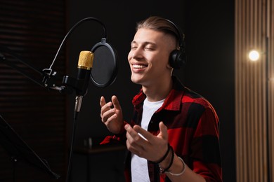 Vocalist with headphones singing into microphone in professional record studio