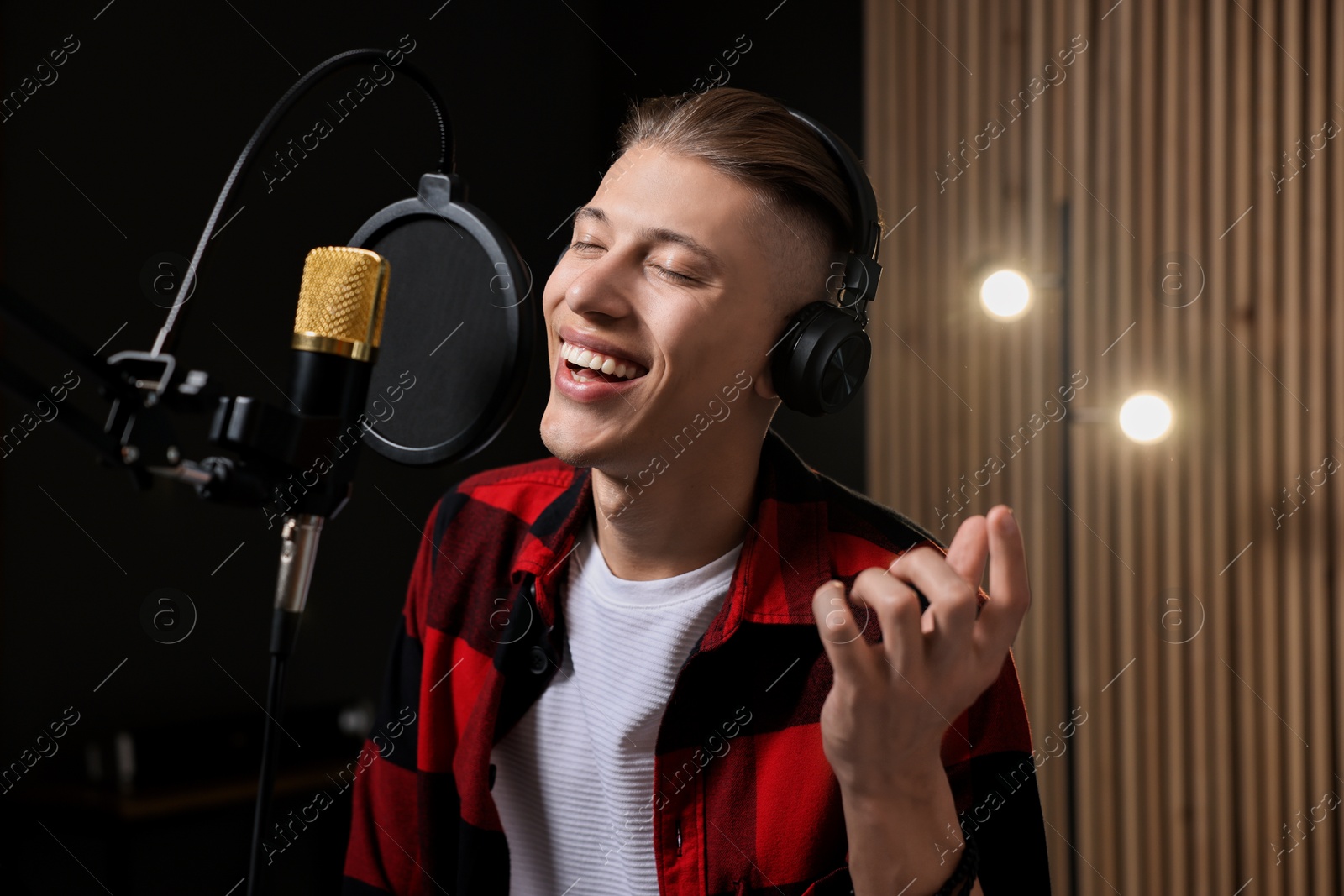 Photo of Vocalist with headphones singing into microphone in professional record studio