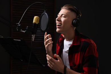 Photo of Vocalist with headphones singing into microphone in professional record studio