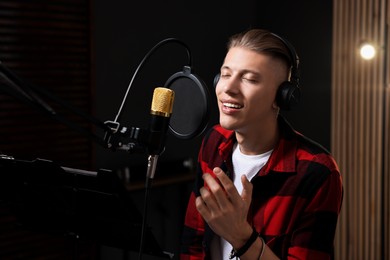 Photo of Vocalist with headphones singing into microphone in professional record studio