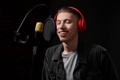 Photo of Vocalist with headphones singing into microphone in professional record studio