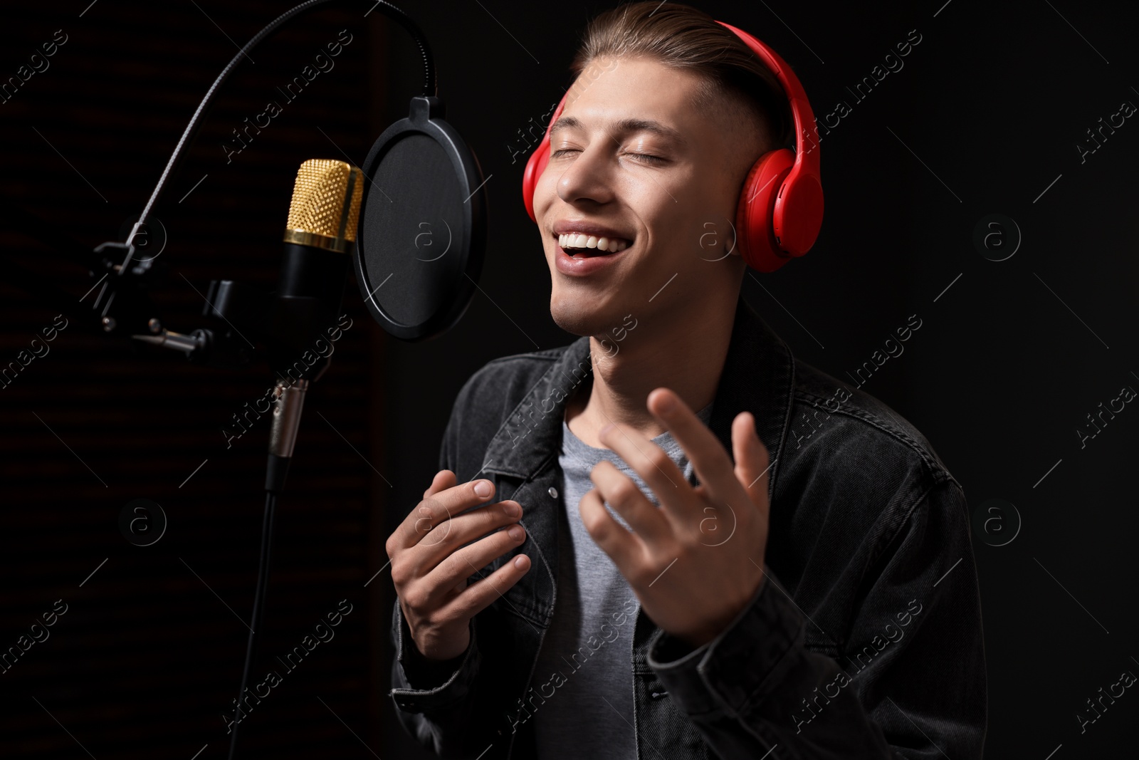 Photo of Man wearing headphones singing into microphone in professional record studio