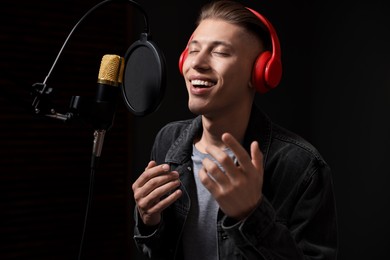 Photo of Man wearing headphones singing into microphone in professional record studio