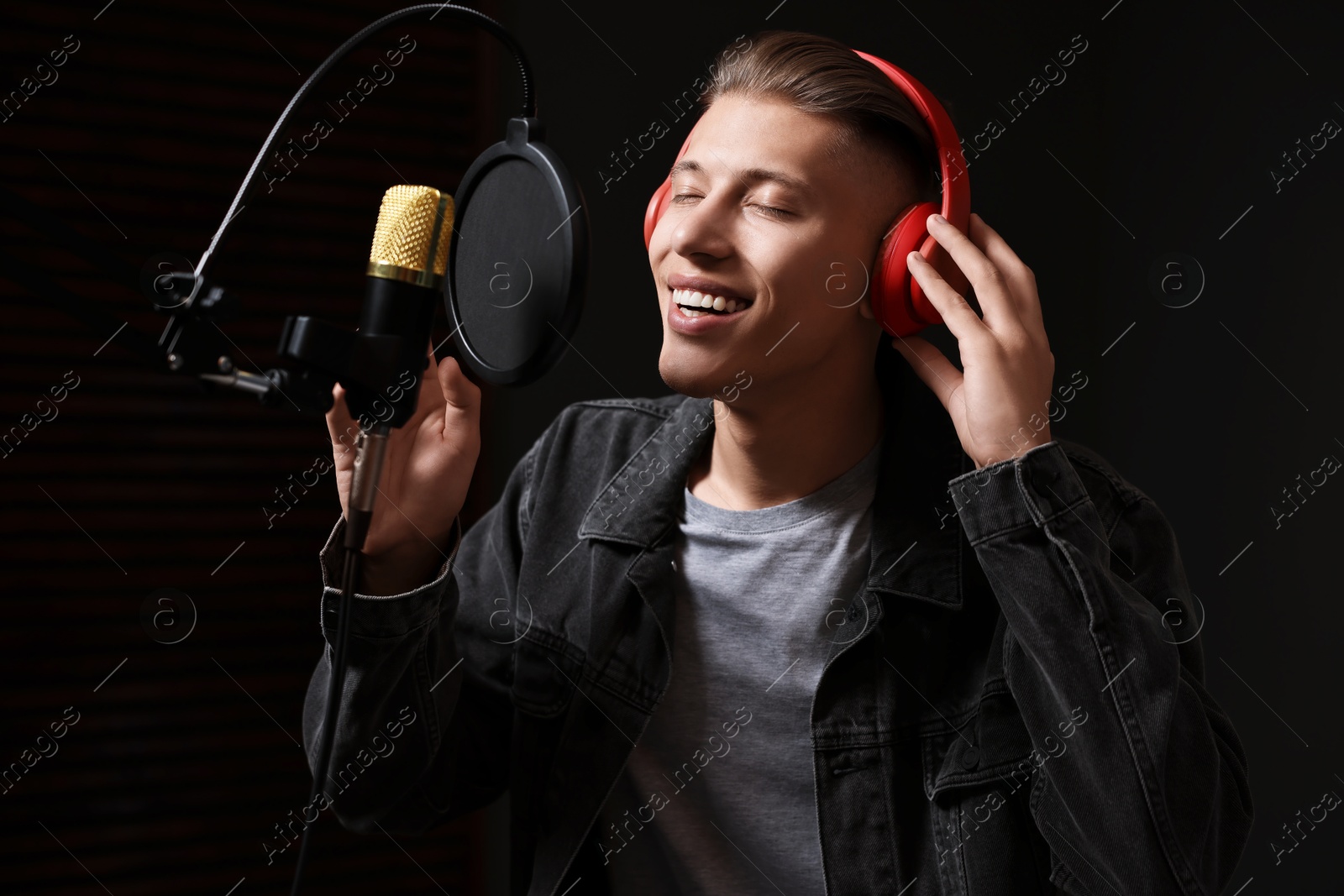 Photo of Man wearing headphones singing into microphone in professional record studio