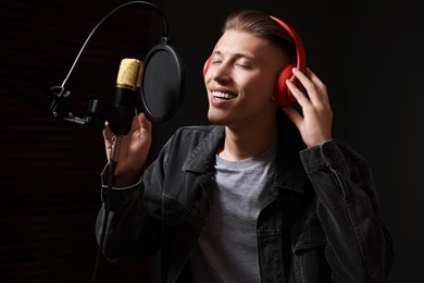 Photo of Man wearing headphones singing into microphone in professional record studio