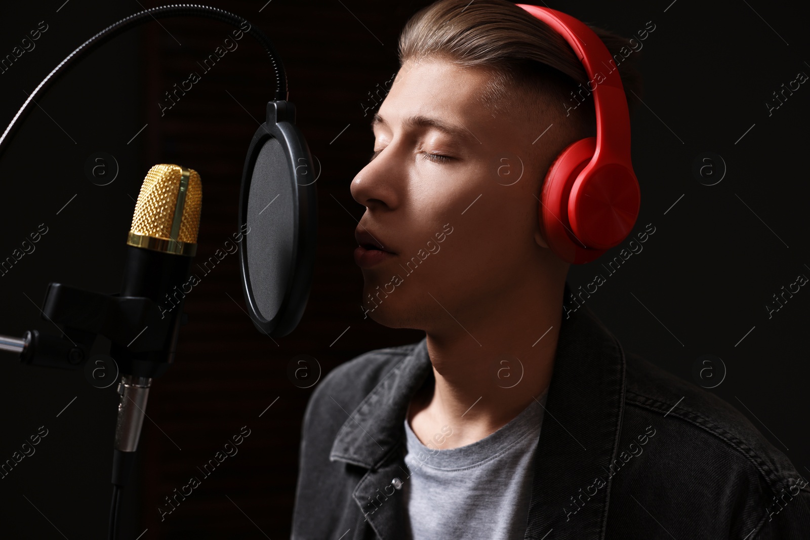 Photo of Vocalist with headphones singing into microphone in professional record studio