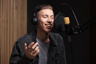 Photo of Vocalist with headphones singing into microphone in professional record studio