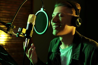 Photo of Vocalist with headphones singing into microphone in professional record studio