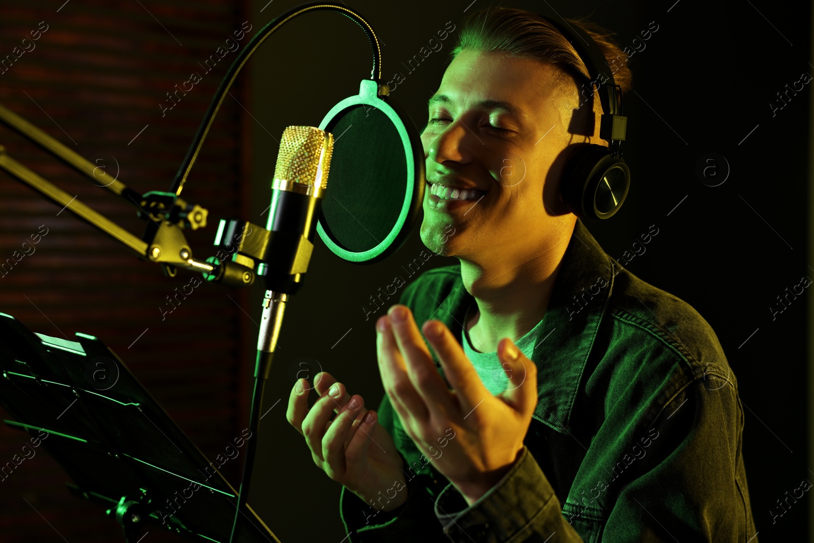 Photo of Vocalist with headphones singing into microphone in professional record studio