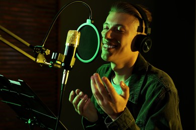 Photo of Vocalist with headphones singing into microphone in professional record studio