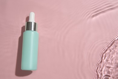 Photo of Bottle of cosmetic product in water on pink background, top view. Space for text