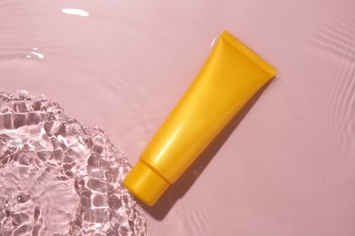 Photo of Cosmetic product. Tube with cream in water on pink background, top view