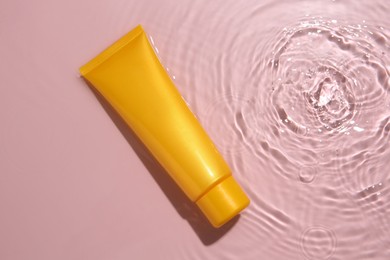 Cosmetic product. Tube with cream in water on pink background, top view