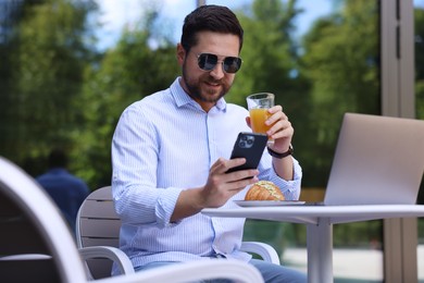 Happy man using smartphone during breakfast in outdoor cafe