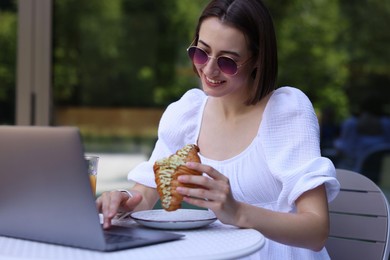 Photo of Happy woman having tasty breakfast and using laptop in outdoor cafe