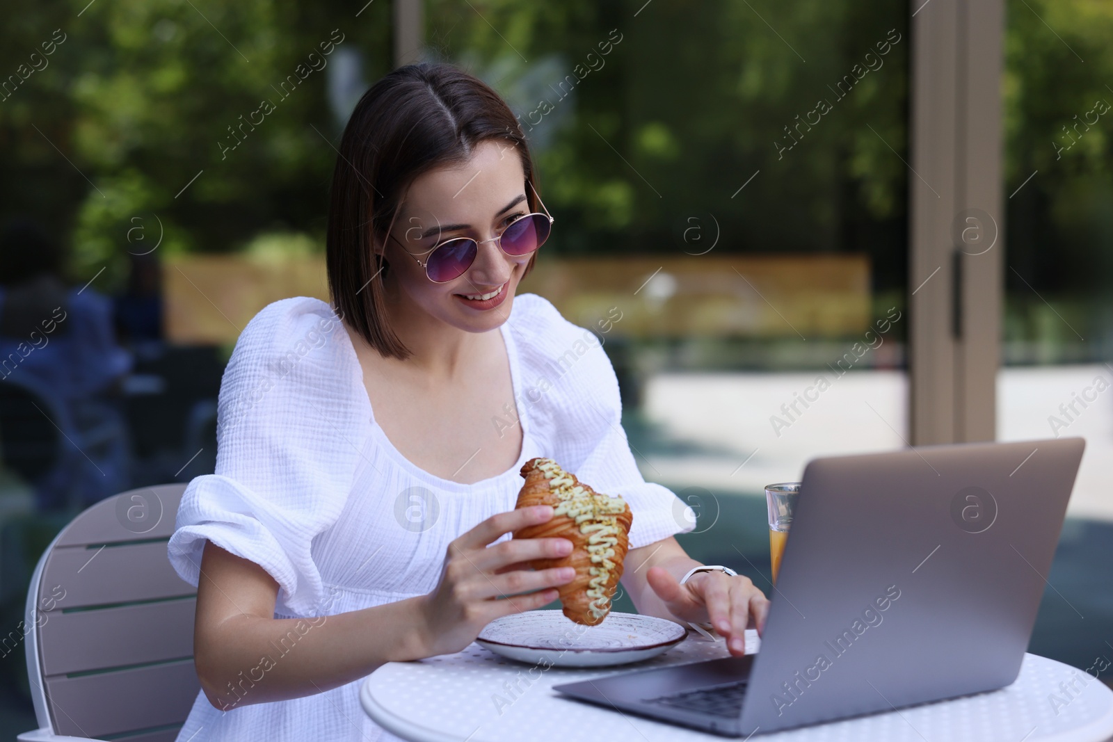 Photo of Happy woman having tasty breakfast and using laptop in outdoor cafe