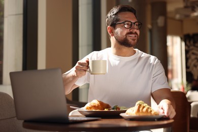 Happy man having tasty breakfast in cafe