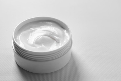 Photo of Face cream in jar on white textured table, closeup. Space for text