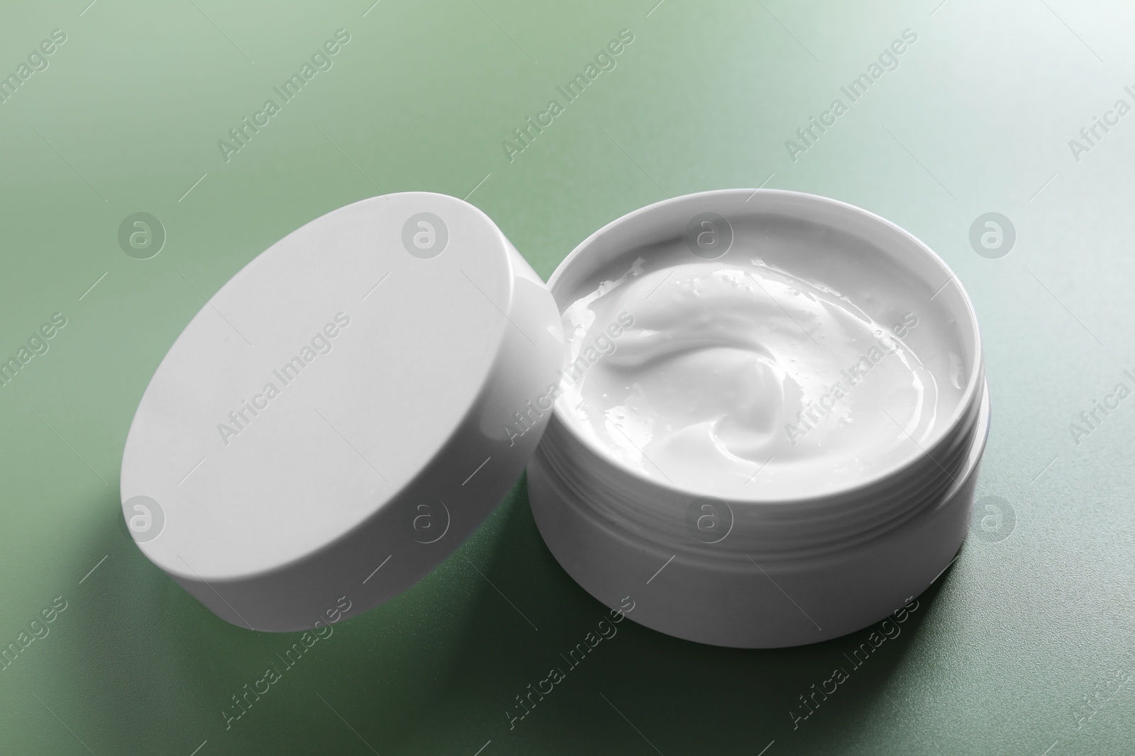 Photo of Face cream in jar on green background, closeup