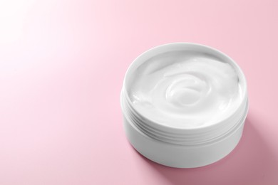 Face cream in jar on pink background, closeup. Space for text