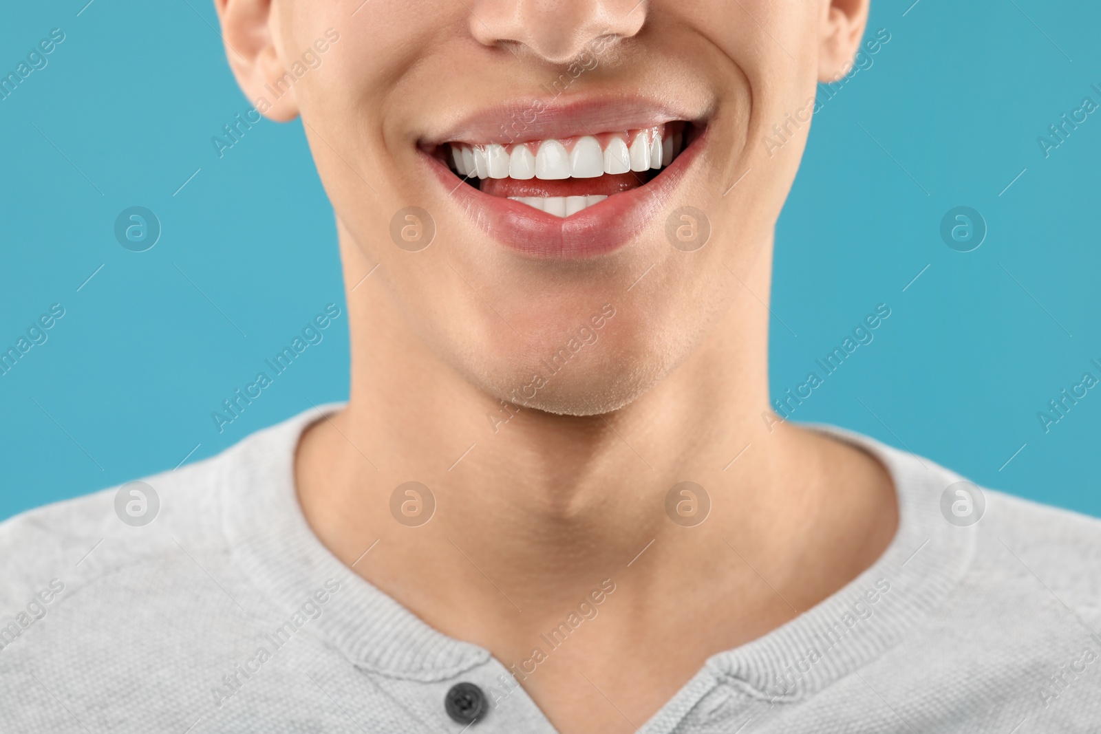 Photo of Happy young man on light blue background, closeup. Dental veneers