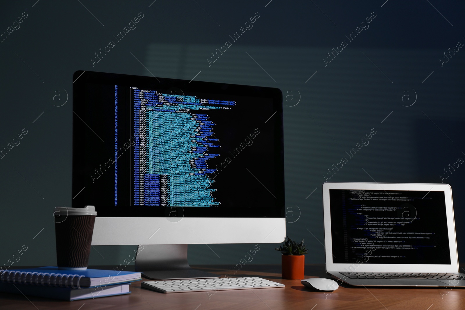 Photo of Programmer's workplace. Modern computer with unfinished code, laptop and other supplies on wooden desk