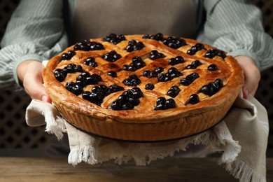 Photo of Woman holding tasty homemade pie with blueberries over wooden table, closeup