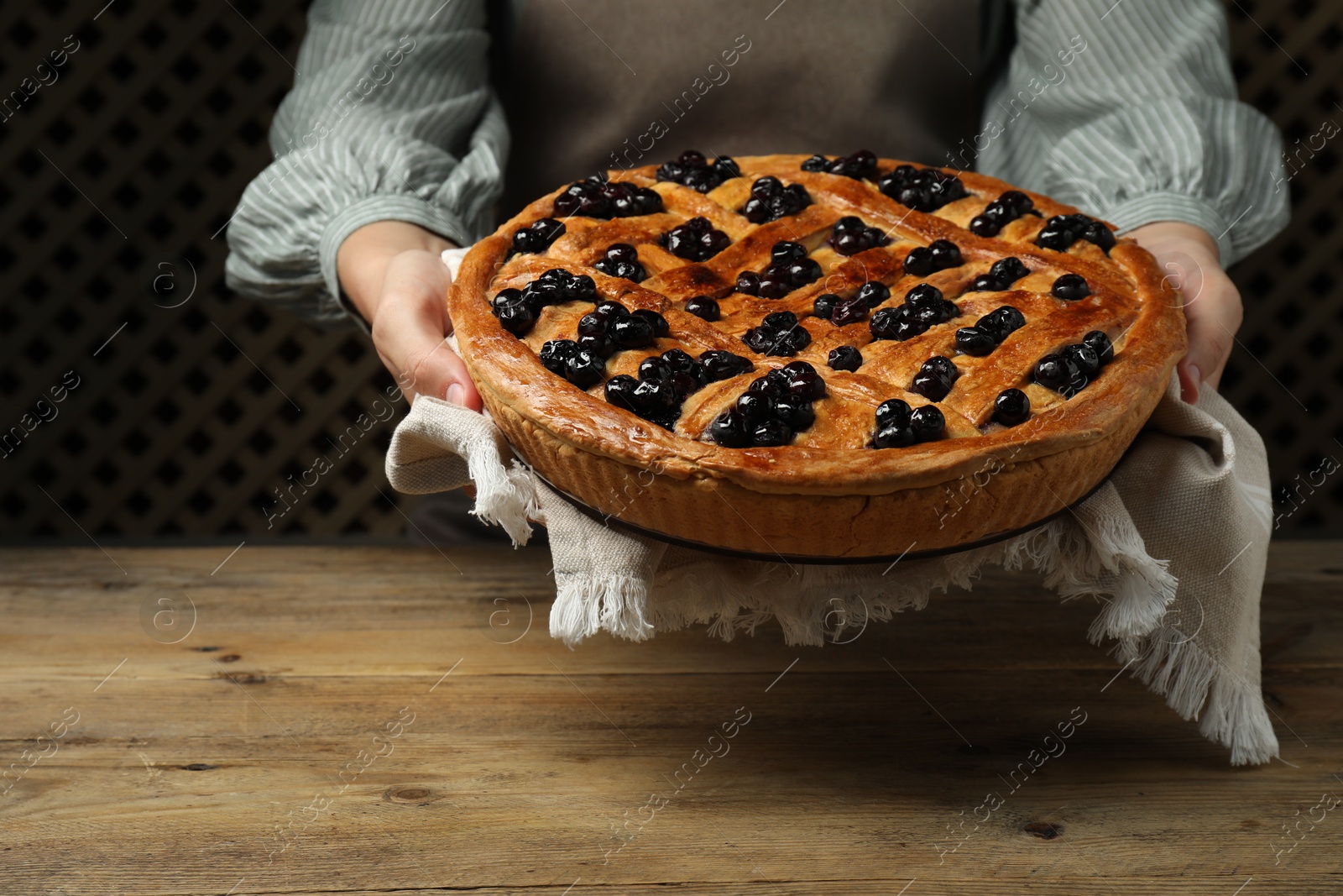 Photo of Woman holding tasty homemade pie with blueberries over wooden table, closeup