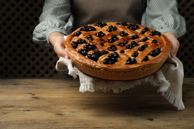 Photo of Woman holding tasty homemade pie with blueberries over wooden table, closeup