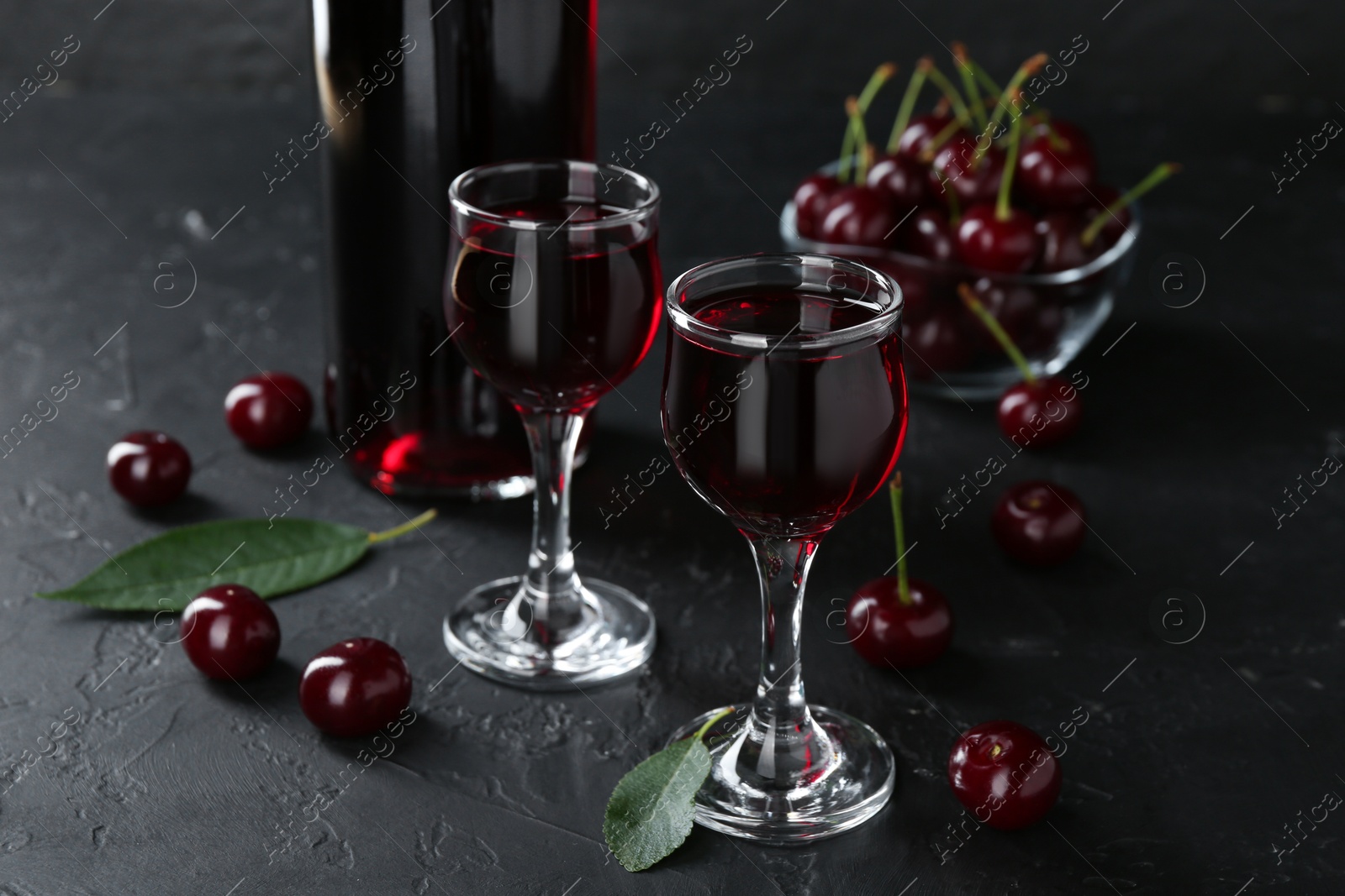 Photo of Delicious cherry liqueur and berries on black table